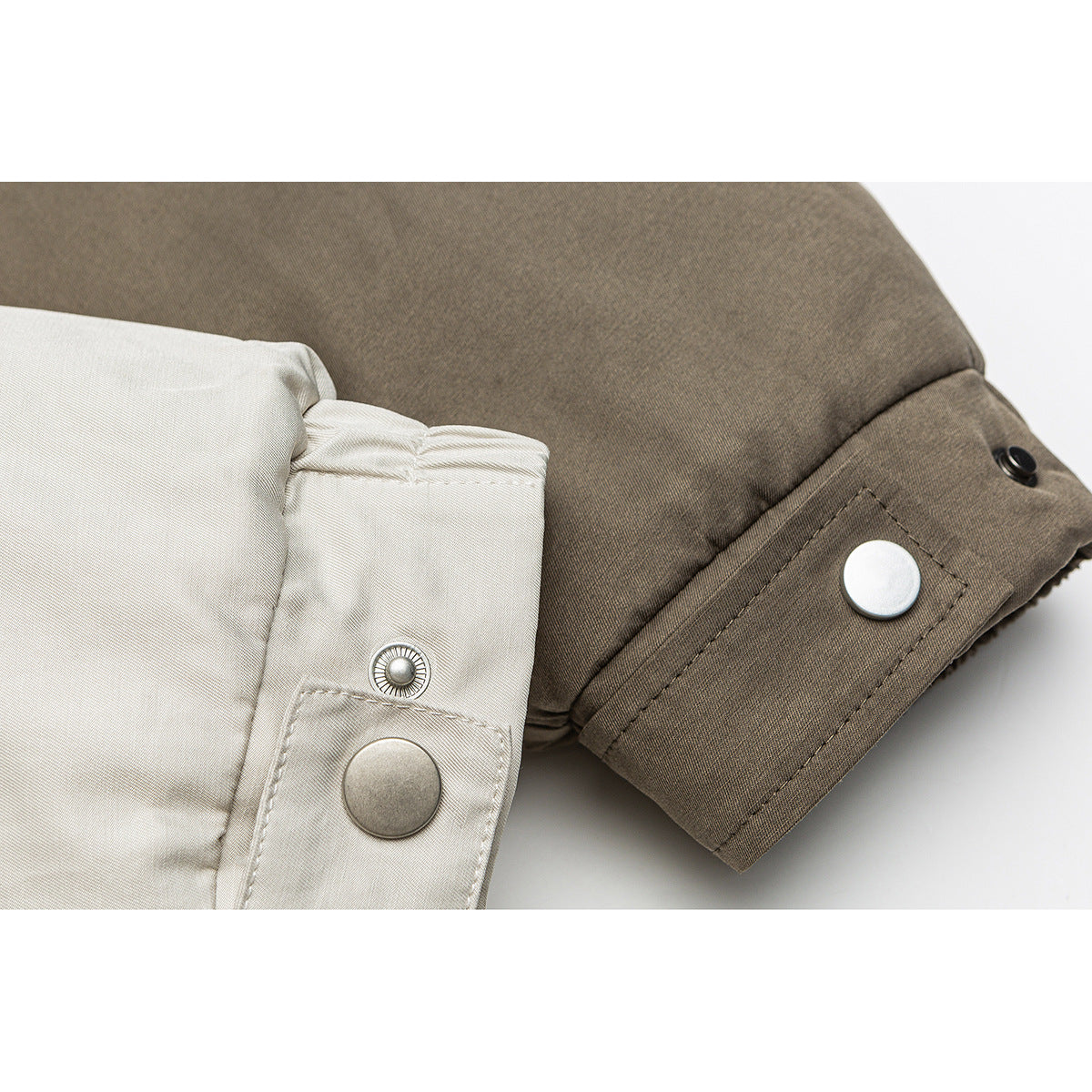 Close-up of a beige jacket sleeve and cuff with metal snap buttons and a dark brown panel.