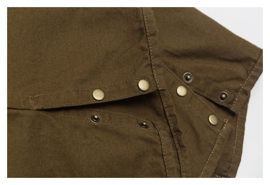 Close-up of dark olive-brown garment fabric with brass-tone snaps, dark eyelets and stitching.