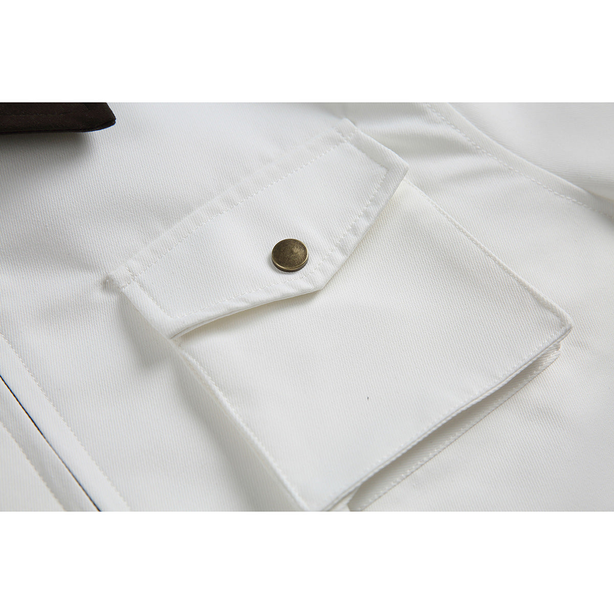 Close-up of a white garment's flap pocket with a round antique-brass button.