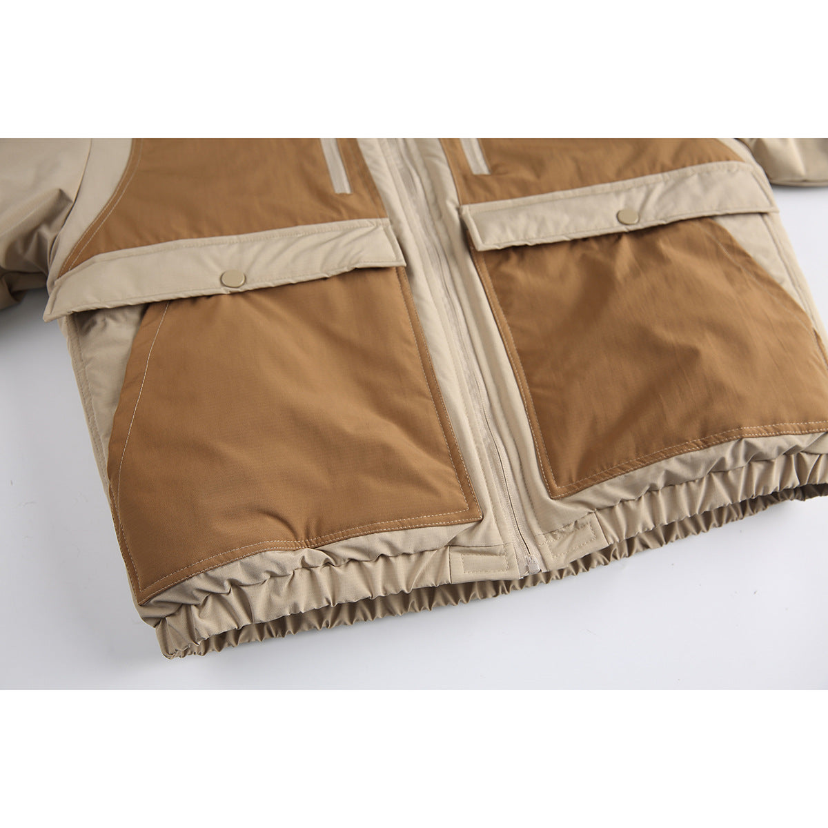 Close-up of the jacket's lower front, showing large brown pockets with beige snap-tab flaps and a gathered hem.
