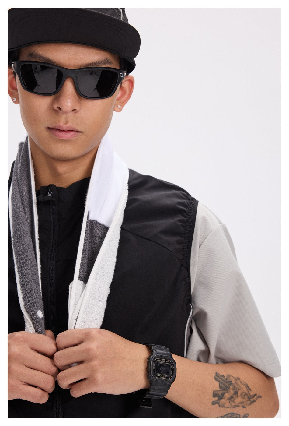 Close-up of a model in a black vest over a gray shirt, with a white and gray towel draped around his neck.