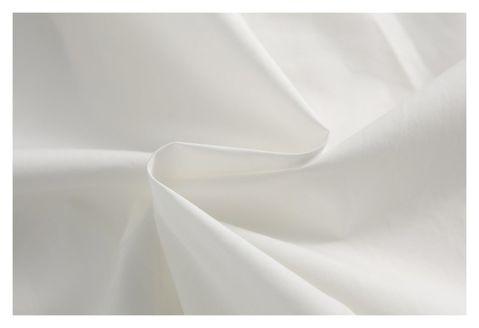 Close-up of white fabric draped in soft folds, showing its fine surface texture.