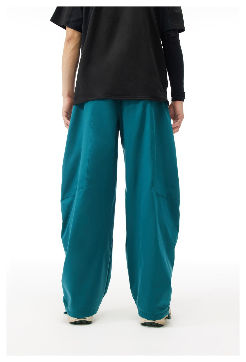 Rear view of a model wearing loose teal pants with plain back panels and adjustable ankle hems.