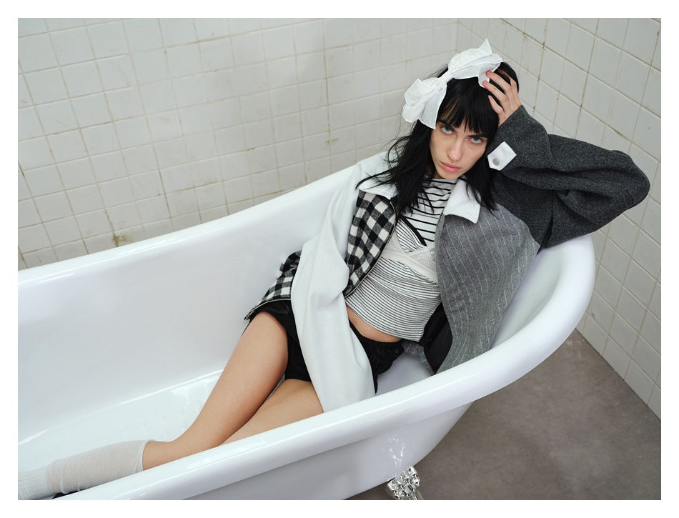 Model reclining in a white bathtub wearing the gingham, pinstripe and gray colorblock jacket over a striped top