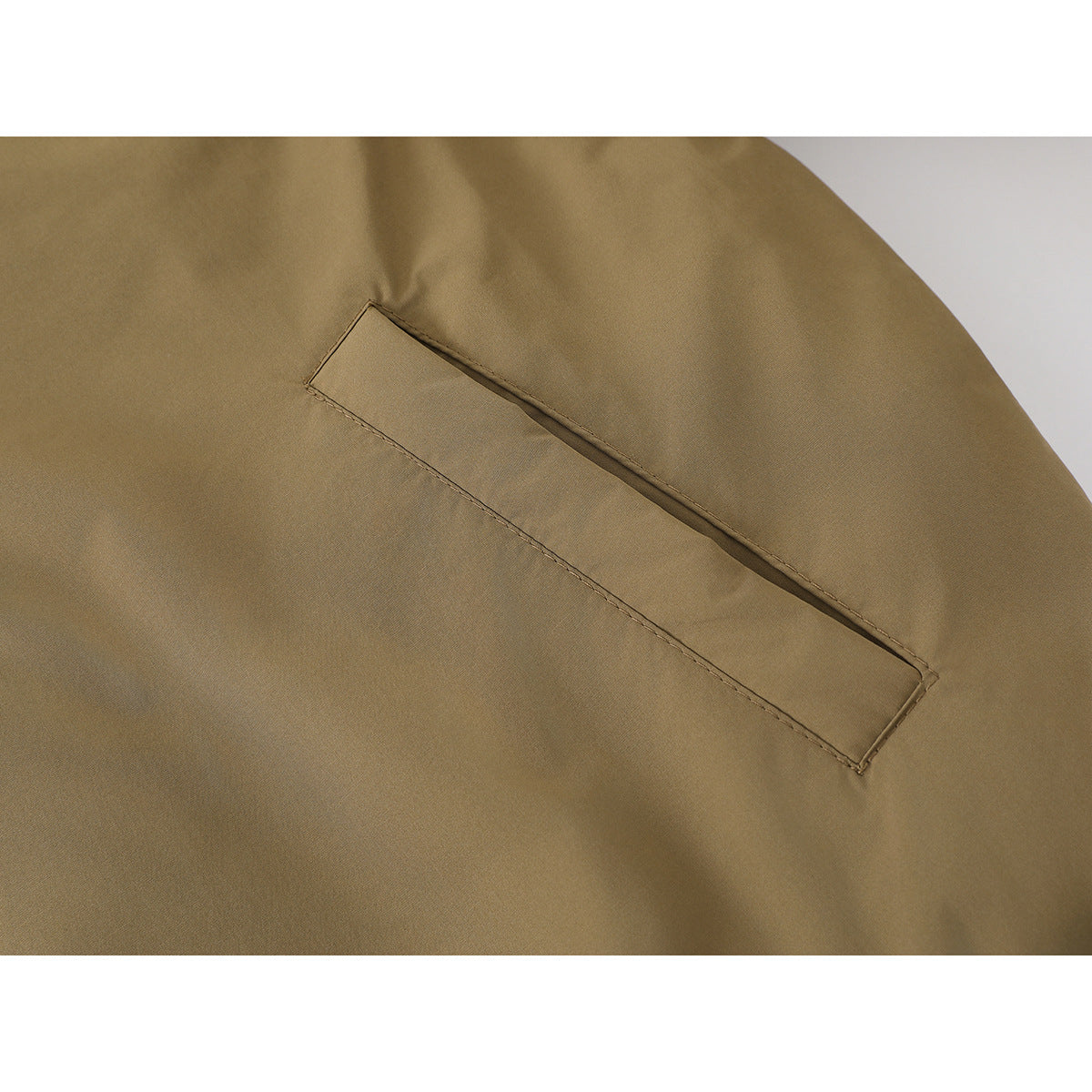 Close-up of a tan jacket's long narrow welt pocket and surrounding fabric.