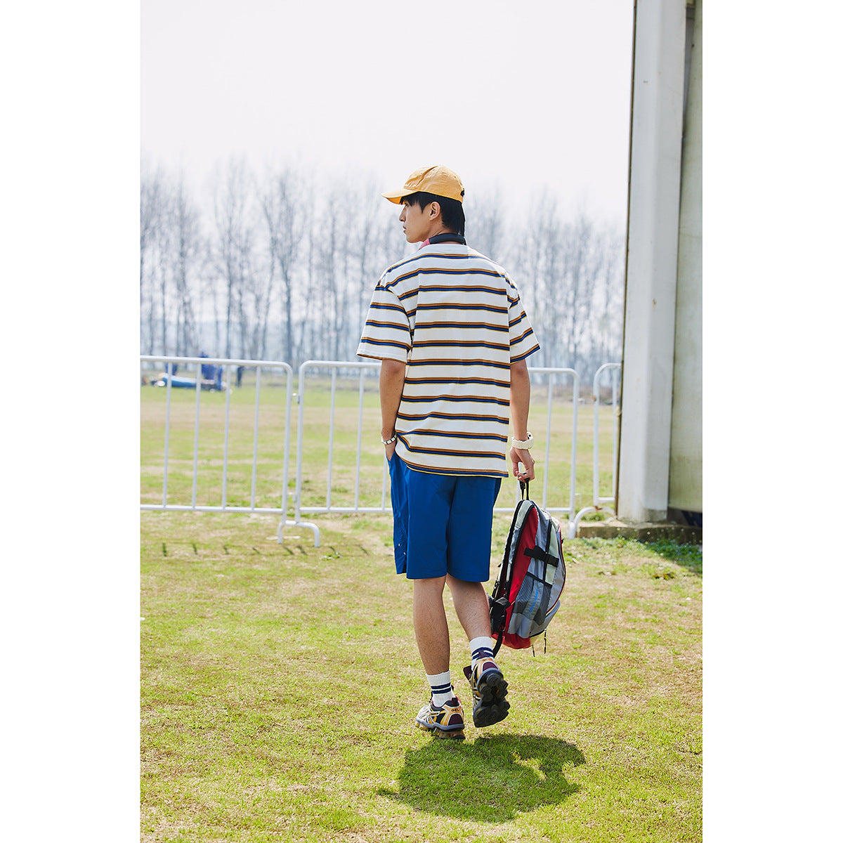 Rear view of a man wearing a white striped T-shirt and bright blue shorts outdoors.