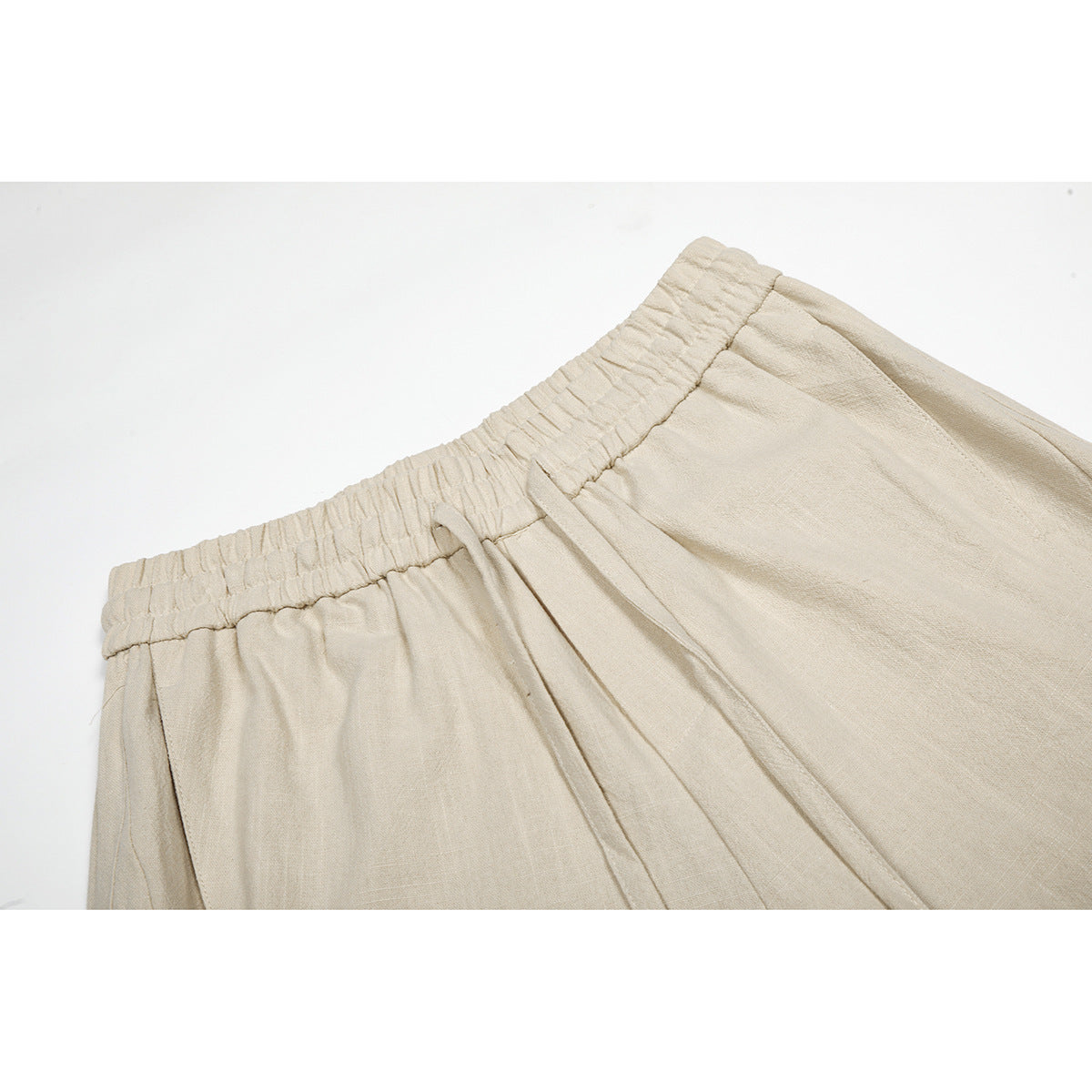 Close-up of beige trousers showing the gathered elastic waistband, front pleats and seam details.