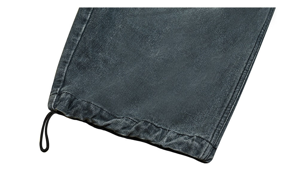 Close-up of a dark gray denim pant leg hem with a black drawcord loop.