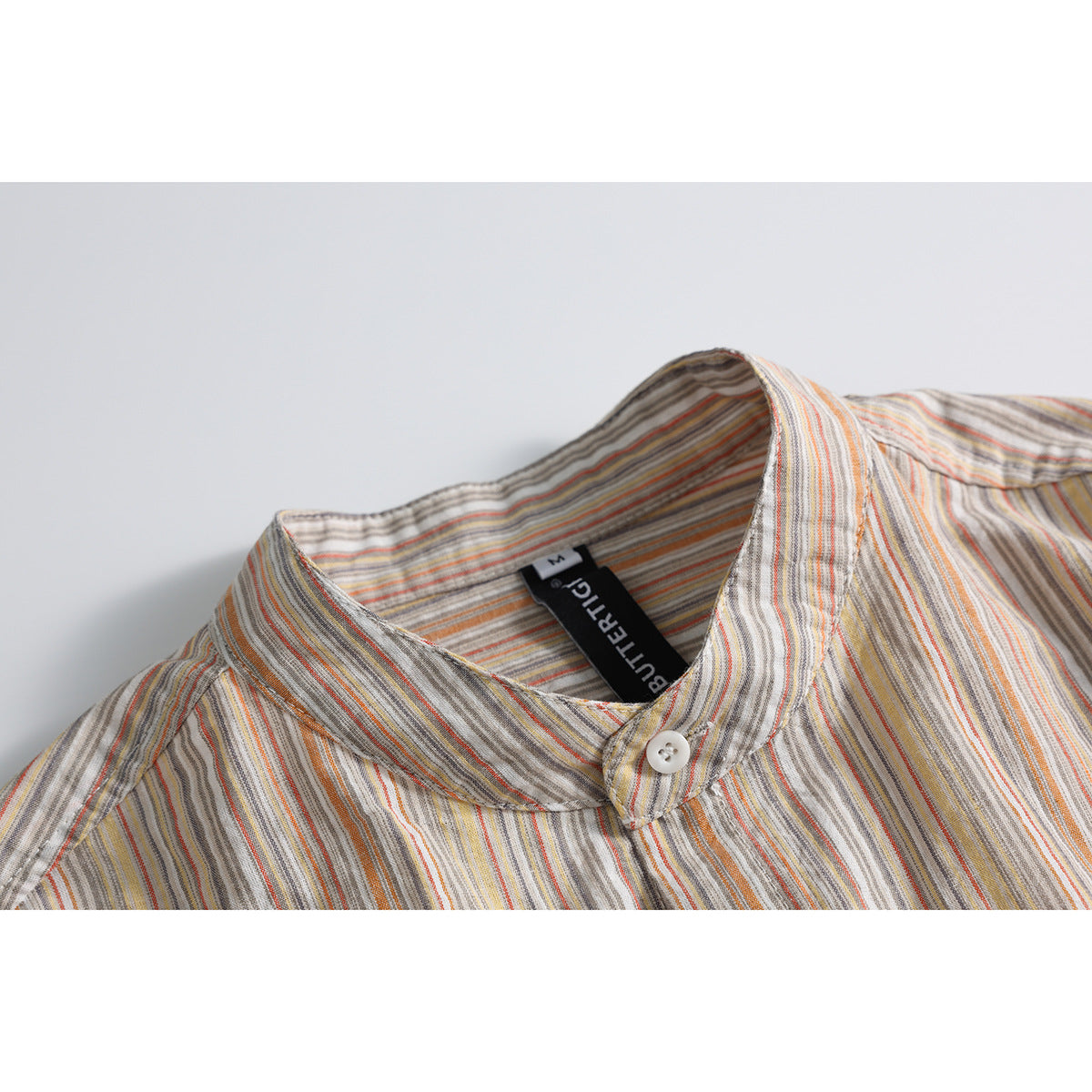 Close-up of a striped shirt’s band collar, button, and inner neck label.