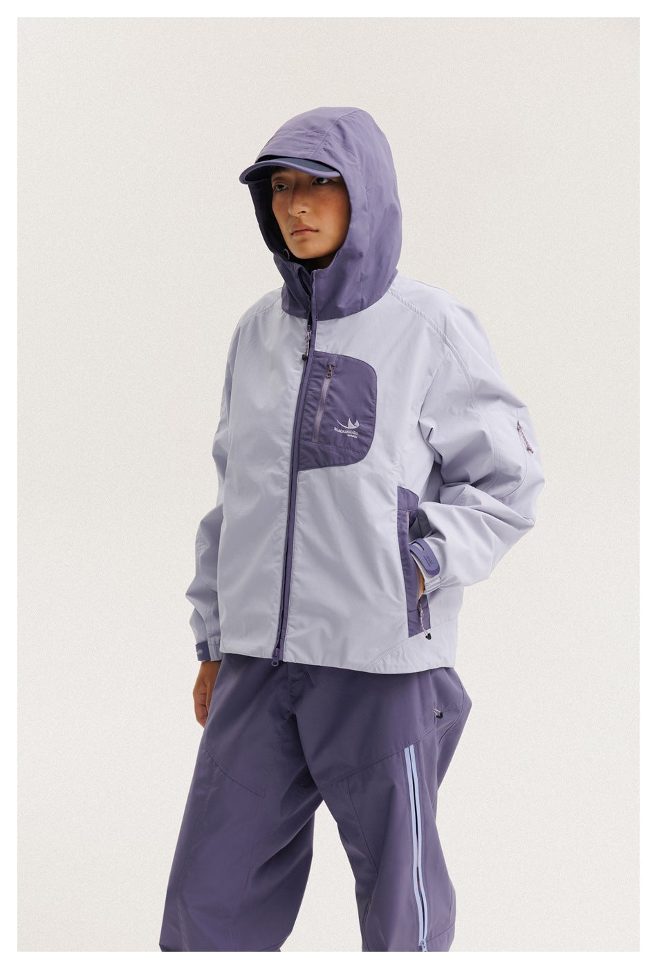 Model wears a light lavender jacket with a purple hood and pocket panels, paired with purple pants.
