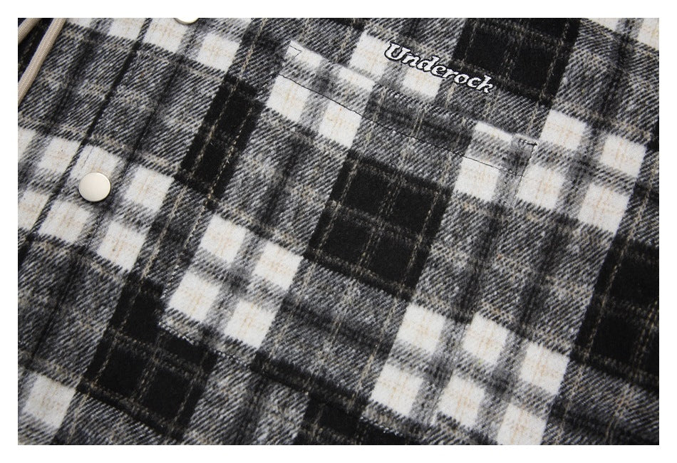 Close-up of a chest pocket, cream snap, and embroidered lettering on plaid fabric.