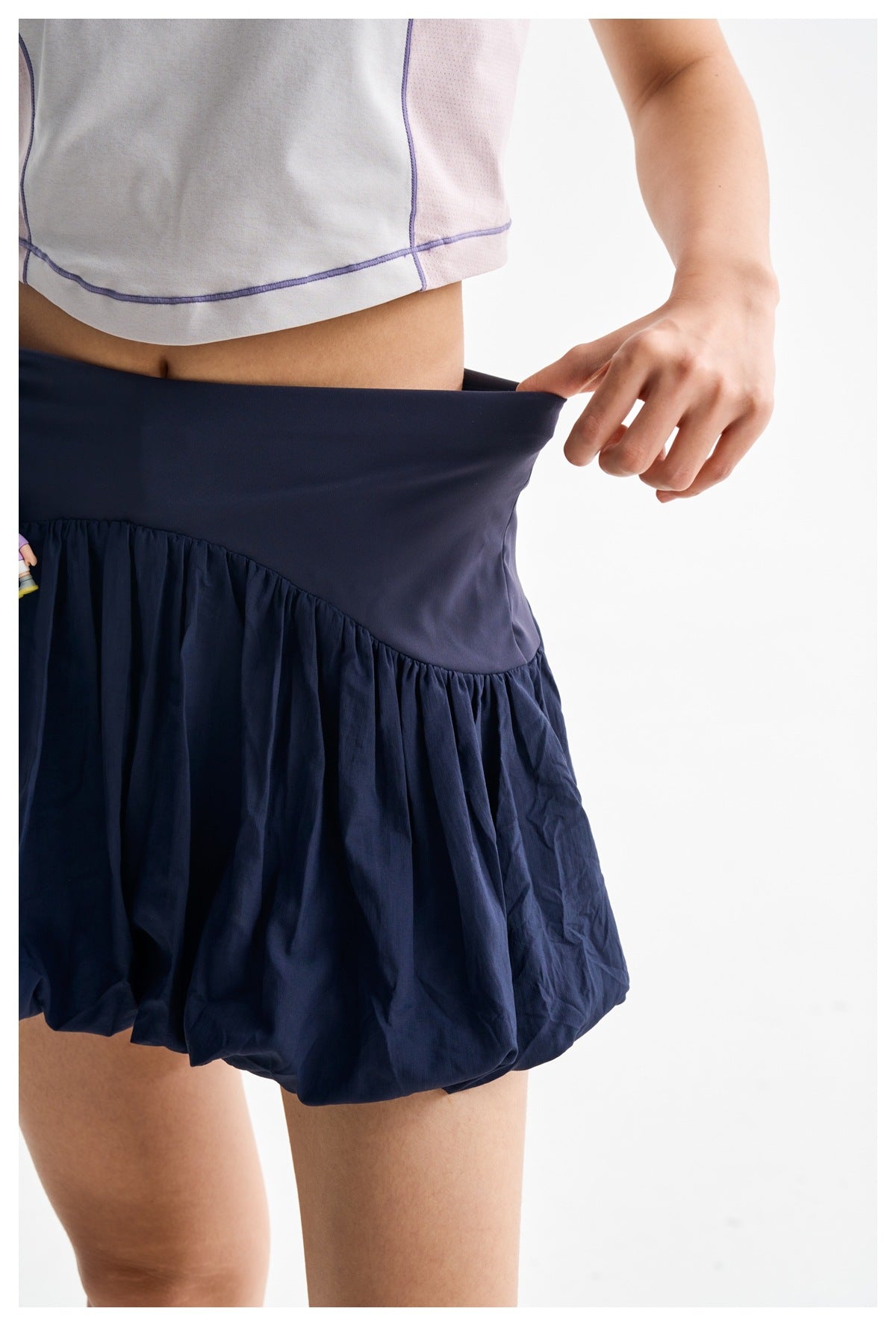 Close-up of a model pulling the wide navy waistband of a bubble-hem skirt outward.