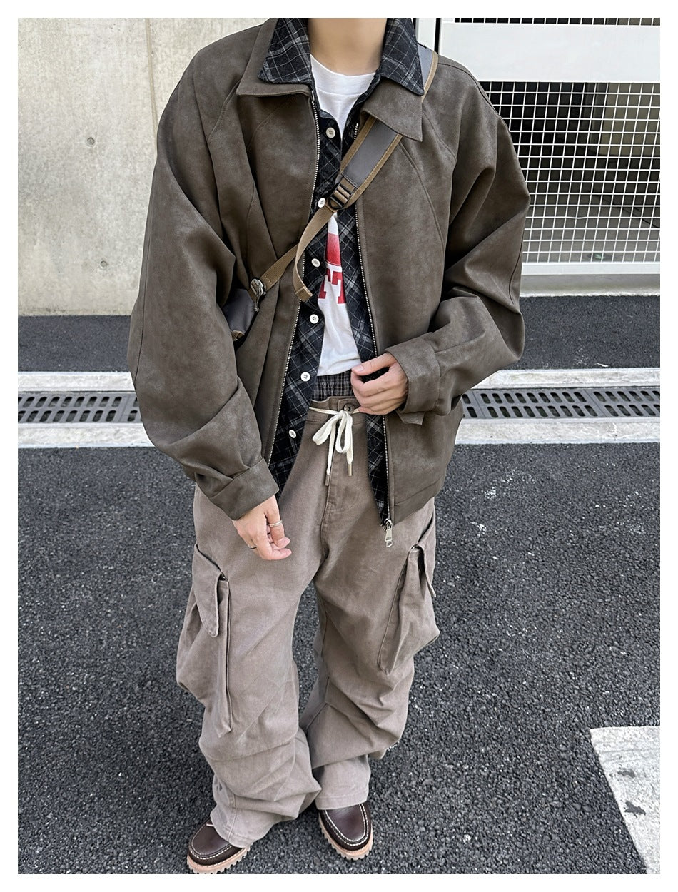 Person wearing a brown faux suede zip jacket over a plaid shirt, white tee and cargo pants, standing outdoors