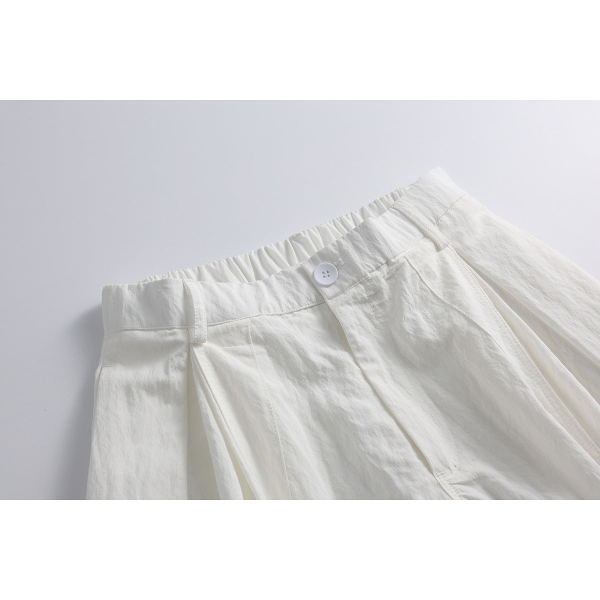 Close-up of white wide-leg pants showing the gathered waistband, button, belt loops and front pleats.