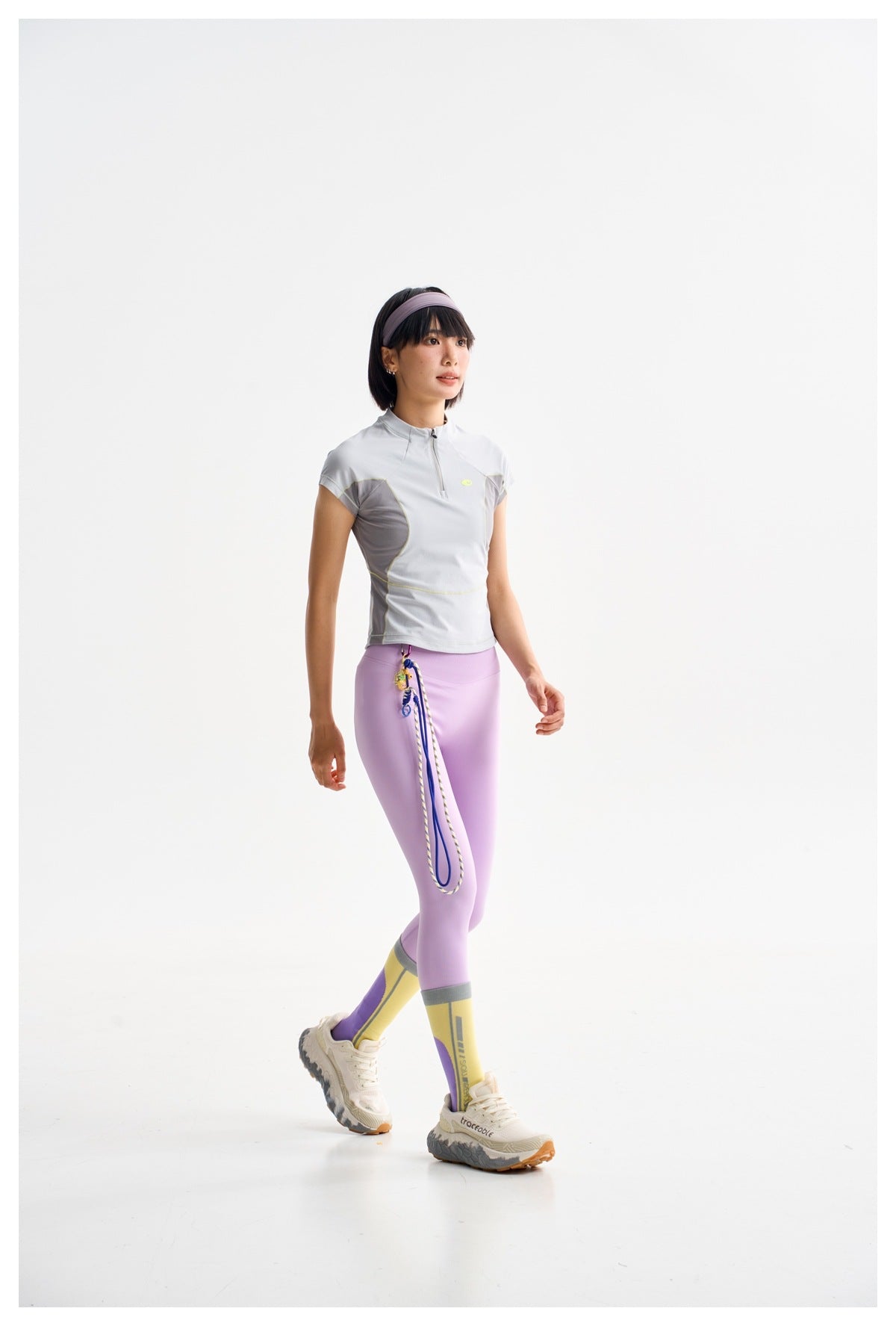 Model wearing a pale gray cap-sleeve quarter-zip top with darker panels and lilac leggings.