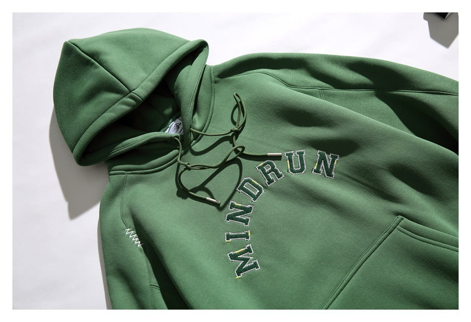 Angled flat lay of a green pullover hoodie with drawstrings, kangaroo pocket, and arched embroidered lettering.