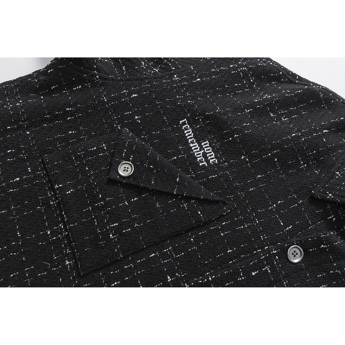 Close-up of a buttoned chest pocket and small white embroidered lettering on a black shirt with a flecked grid pattern.