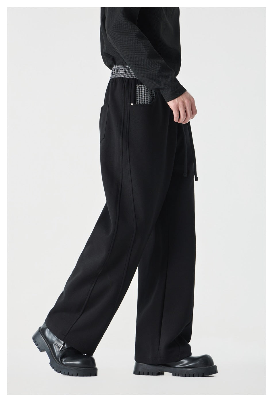 Side view of a model wearing black wide-leg pants with a checked waistband and pocket detail.