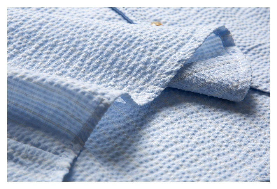 Close-up of a folded sleeve or cuff edge and stitching on the pale blue textured shirt.