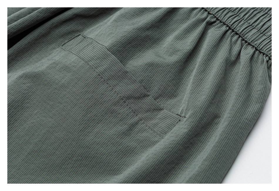 Close-up of a stitched pocket on a blue-gray finely striped garment, with part of the gathered waistband visible.