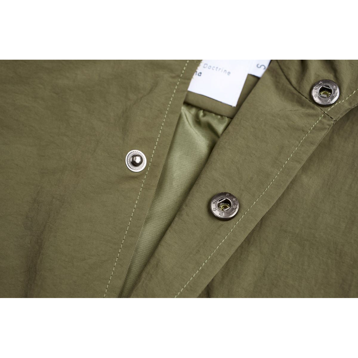Close-up of the olive vest's snap-button placket, stitching, and partially visible inner neck label.