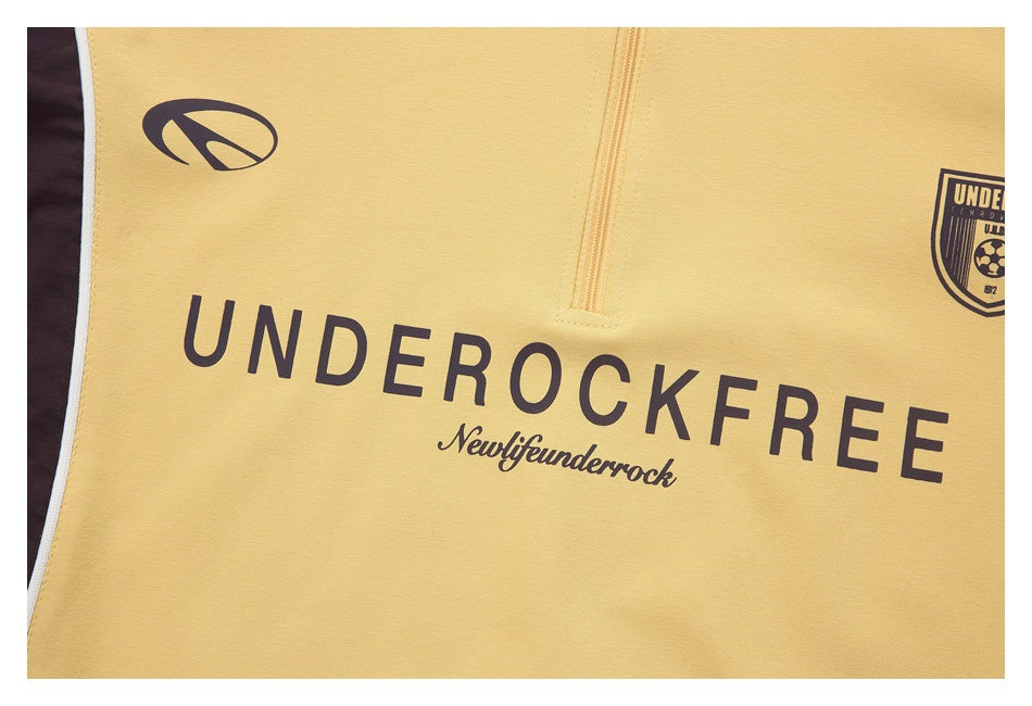 Close-up of pale yellow top showing a short zipper, dark printed lettering and emblems on the front.