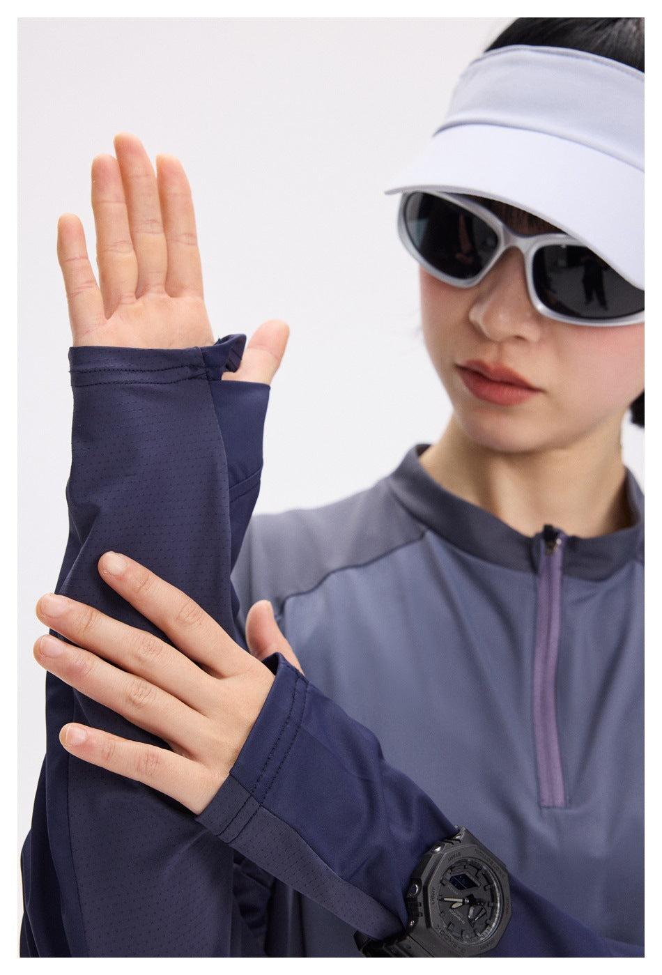 Close-up of a model wearing a slate-blue quarter-zip top and a navy thumbhole sleeve covering the hand.