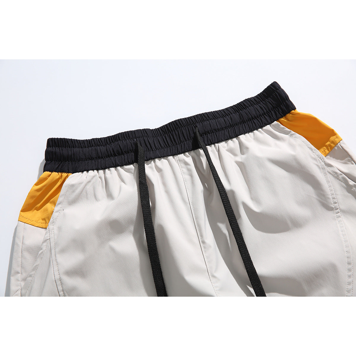 Close-up of light gray shorts with a black elastic drawstring waistband and mustard-yellow side panels.