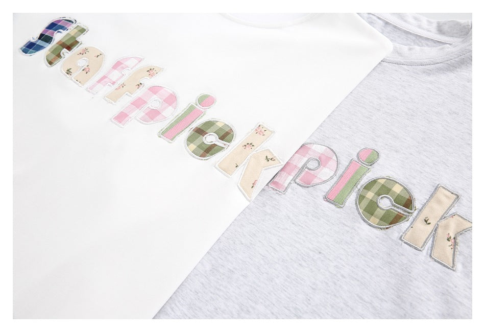 White and light gray T-shirts shown together with large pastel patchwork letters across the chest.