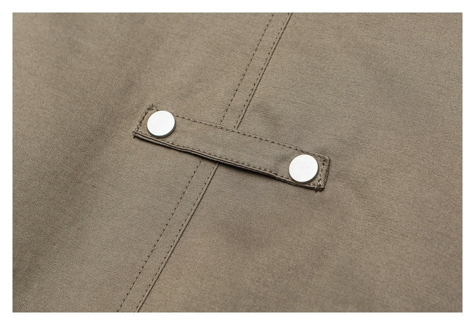 Close-up of a taupe jacket’s fabric fastening tab with two round silver snaps.