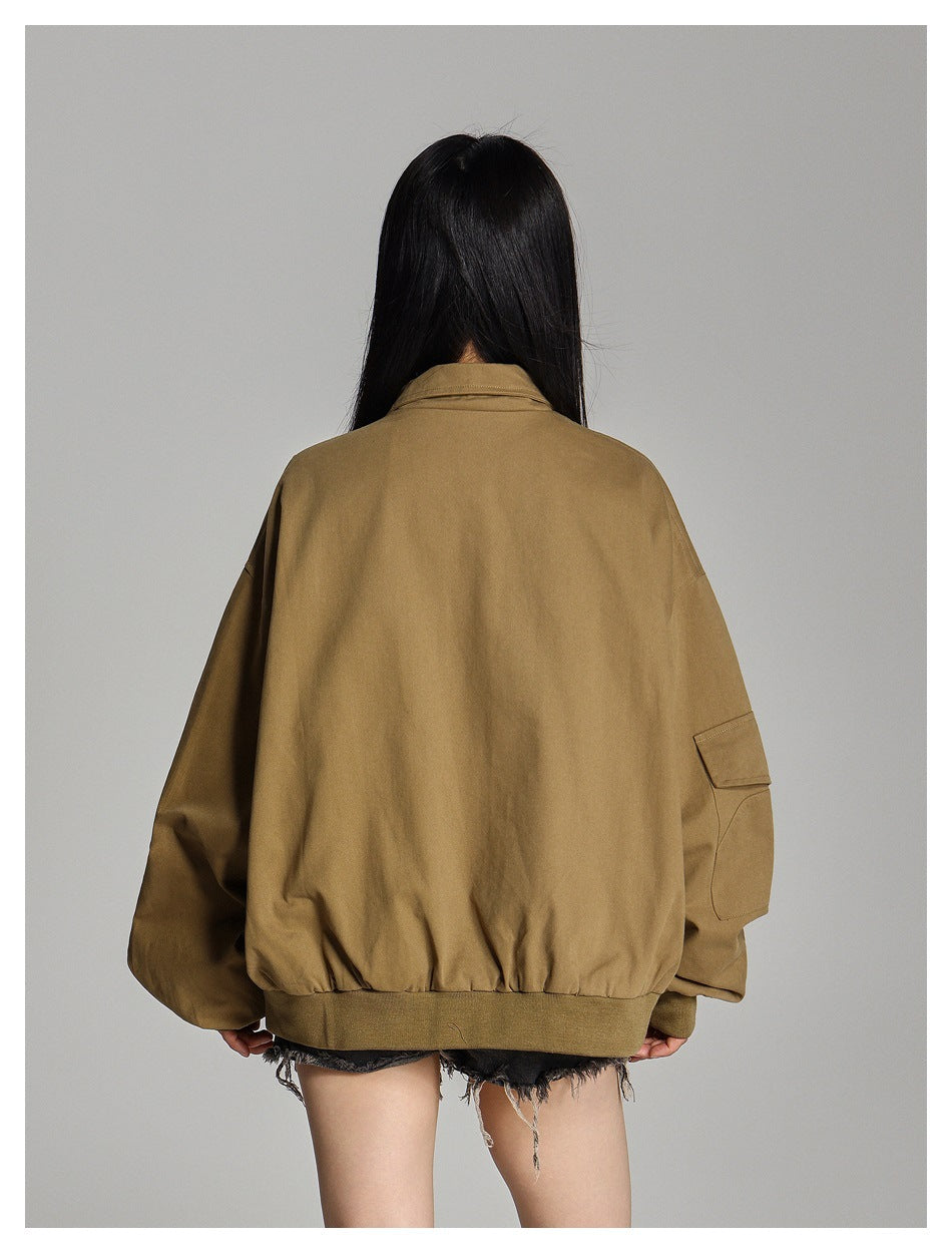 Back view of a model wearing an oversized camel-brown jacket with a ribbed hem and a flap pocket on the sleeve.