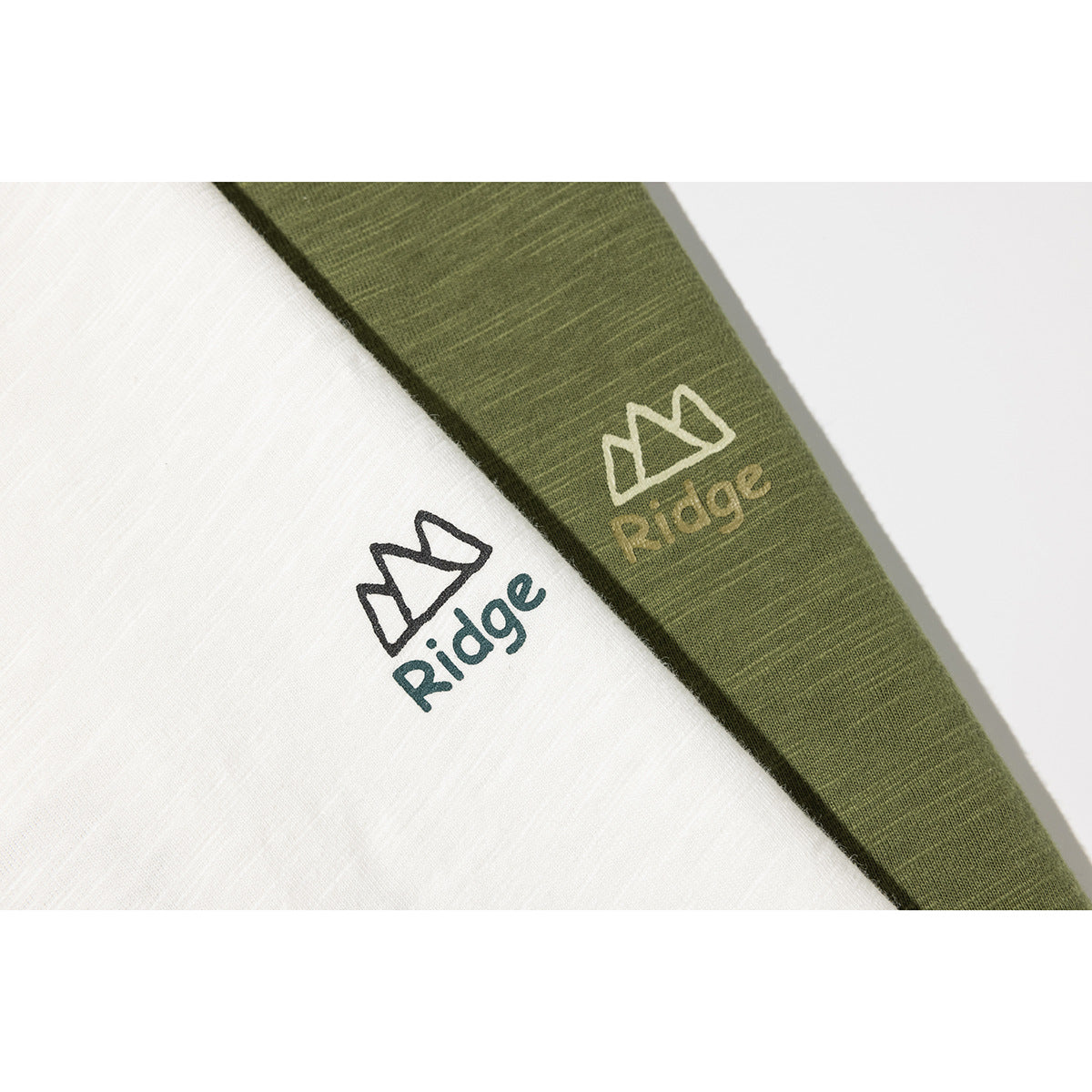 Close-up of white and olive green T-shirts showing small mountain-style Ridge chest logos.