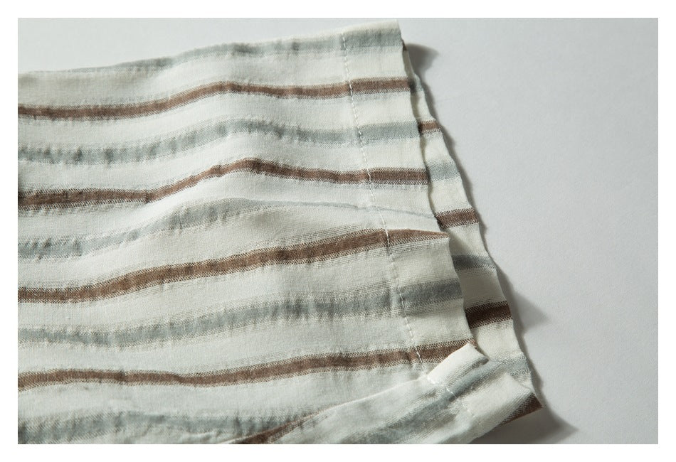 Close-up of a folded hem on off-white fabric with horizontal muted gray and brown stripes.