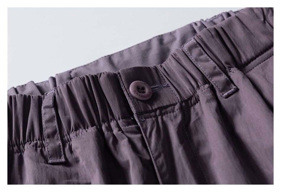 Angled close-up of mauve-gray pants with a gathered waistband, button closure, and belt loops.