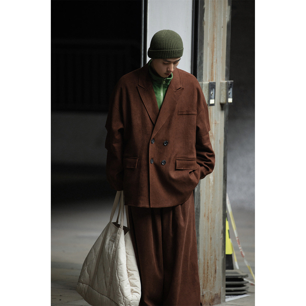 Model wearing an oversized brown double-breasted blazer and wide-leg trousers with a green top and olive beanie.