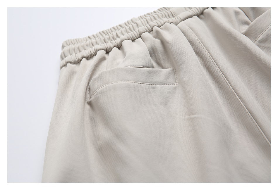 Close-up of a welt pocket and gathered waistband on light beige trousers.