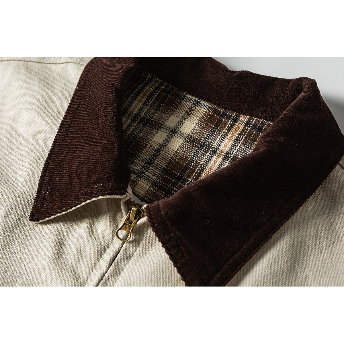 Close-up of an off-white jacket with a dark brown collar, plaid inner lining and brass-tone zipper.