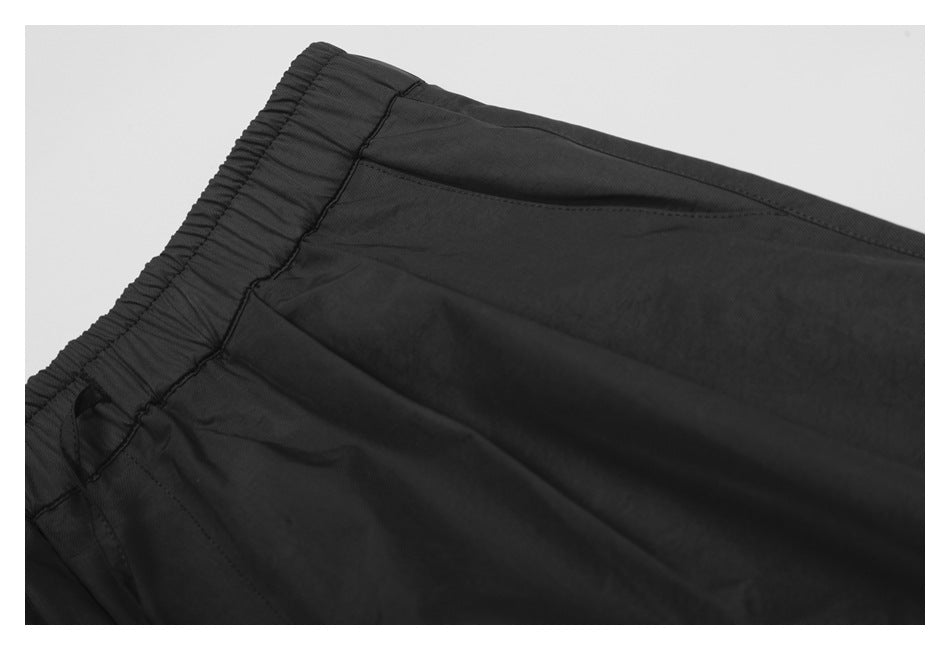Close-up of black pants showing the gathered elastic waistband and curved pocket seam.