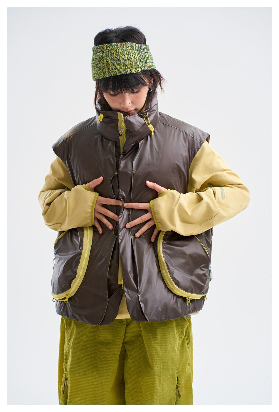 Model wearing a glossy dark brown sleeveless vest with yellow trim over a pale yellow top, shown from the front.