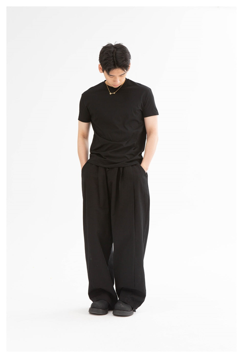 Front view of a model wearing a plain black crew-neck T-shirt and loose black trousers.