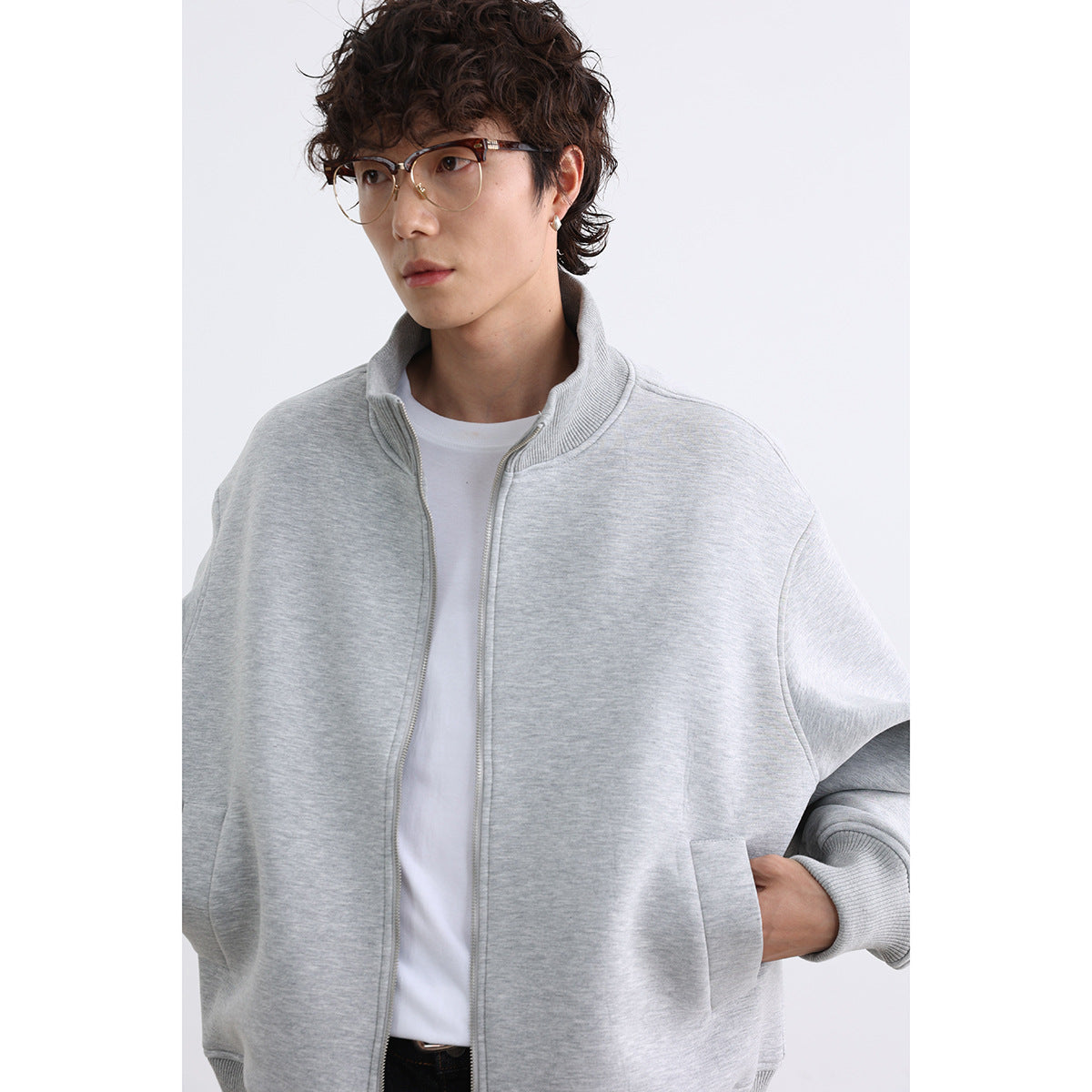 Close-up of a model wearing a light gray zip-front jacket with a ribbed stand collar and front pockets.