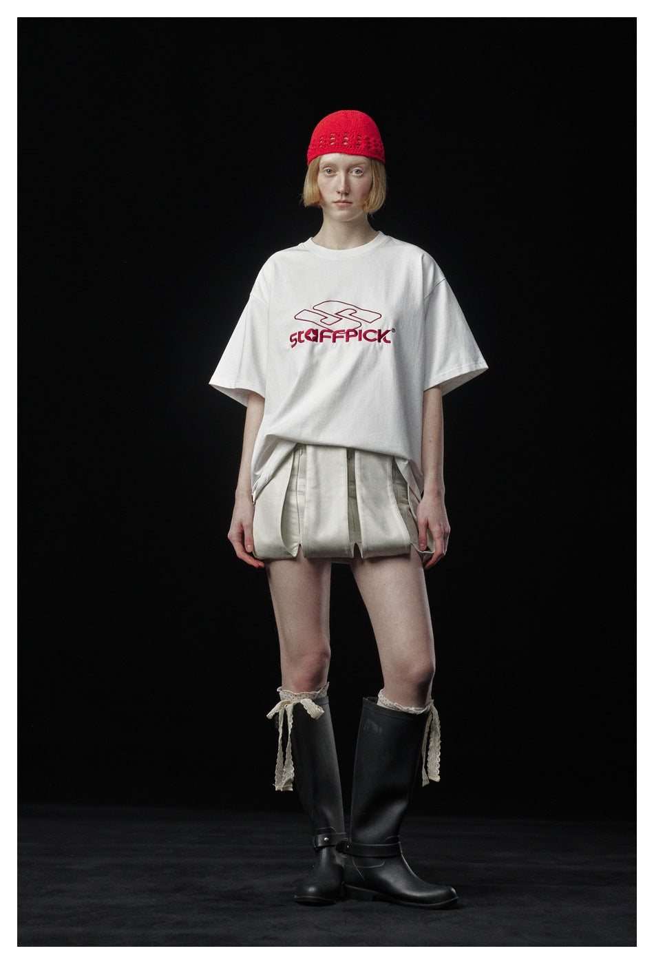 Model wearing a white oversized T-shirt with red embroidered logo, red knit cap, light skirt and black tall boots