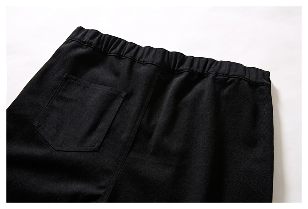 Close-up of the back of black trousers, showing an elastic waistband and a patch pocket.