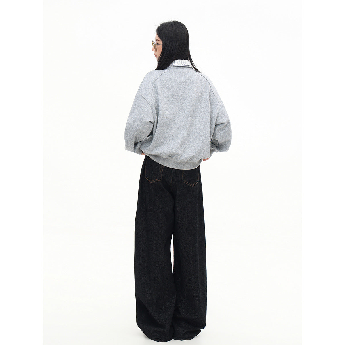Back view of a model wearing a light gray oversized pullover with a striped collar and black wide-leg jeans.