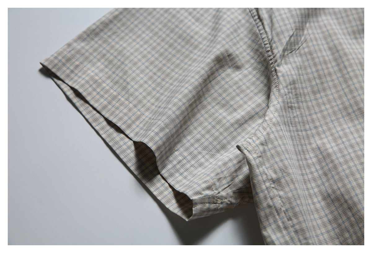 Close-up of the light gray plaid shirt’s short sleeve, hem, and stitching.