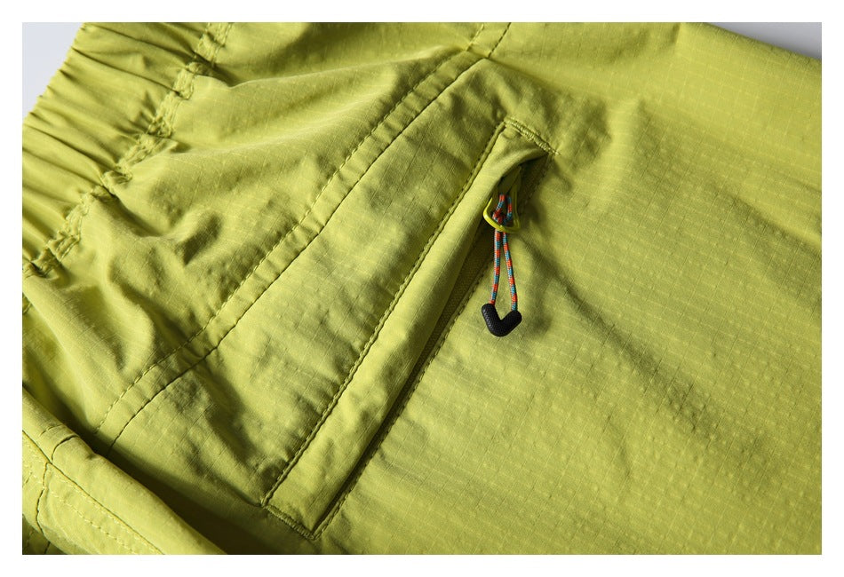 Close-up of a diagonal zip pocket with a multicolor cord pull on lime-yellow shorts.