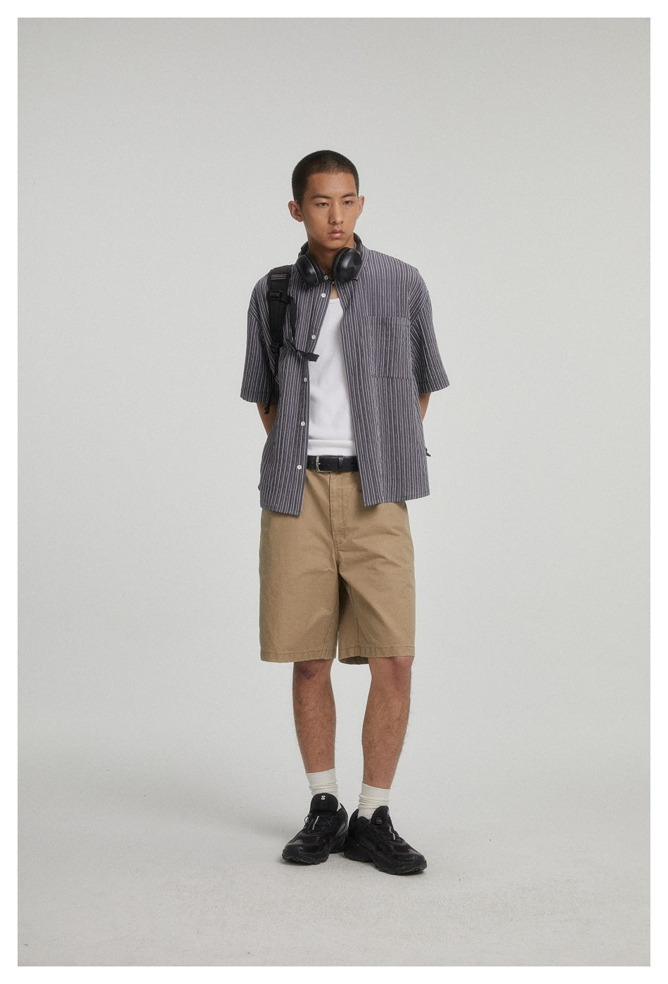 Front view of a model in a charcoal gray pinstriped short-sleeve shirt, white top and tan shorts.