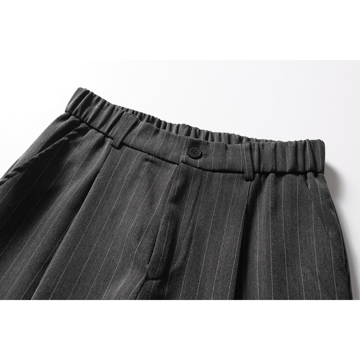 Close-up of charcoal pinstripe trousers showing the gathered waistband, belt loops, button, and front pleats.