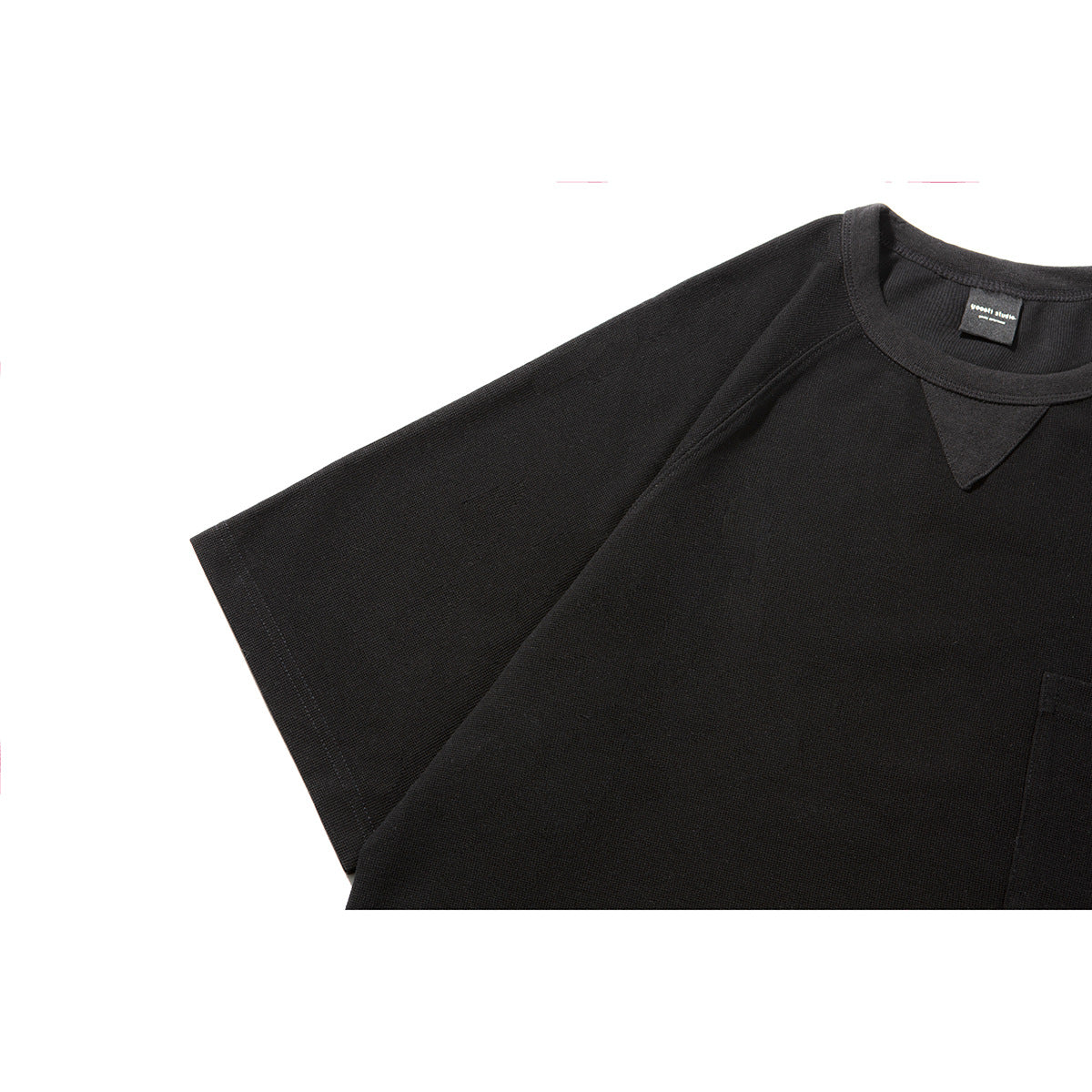 Close-up of a black short-sleeve T-shirt showing its crew neck, triangular insert, raglan seams and pocket edge.