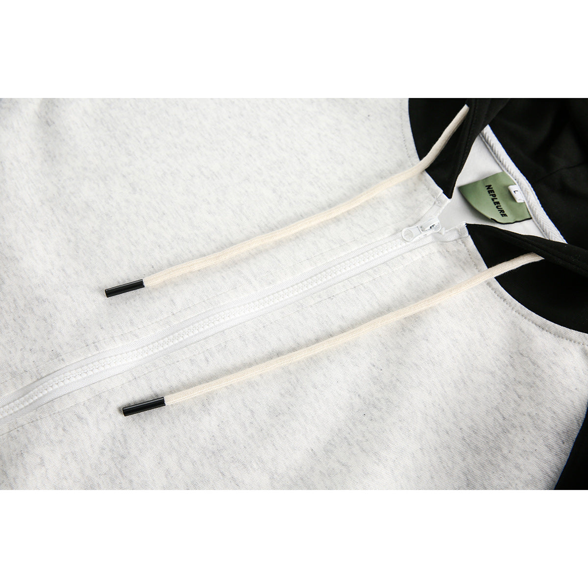 Close-up of a light gray hoodie showing its white front zipper, cream drawstrings, and black hood trim.